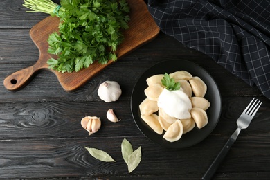 Photo of Delicious cooked dumplings with sour cream on dark wooden table, flat lay