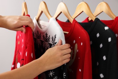 Photo of Woman choosing Christmas sweater from rack near light wall, closeup