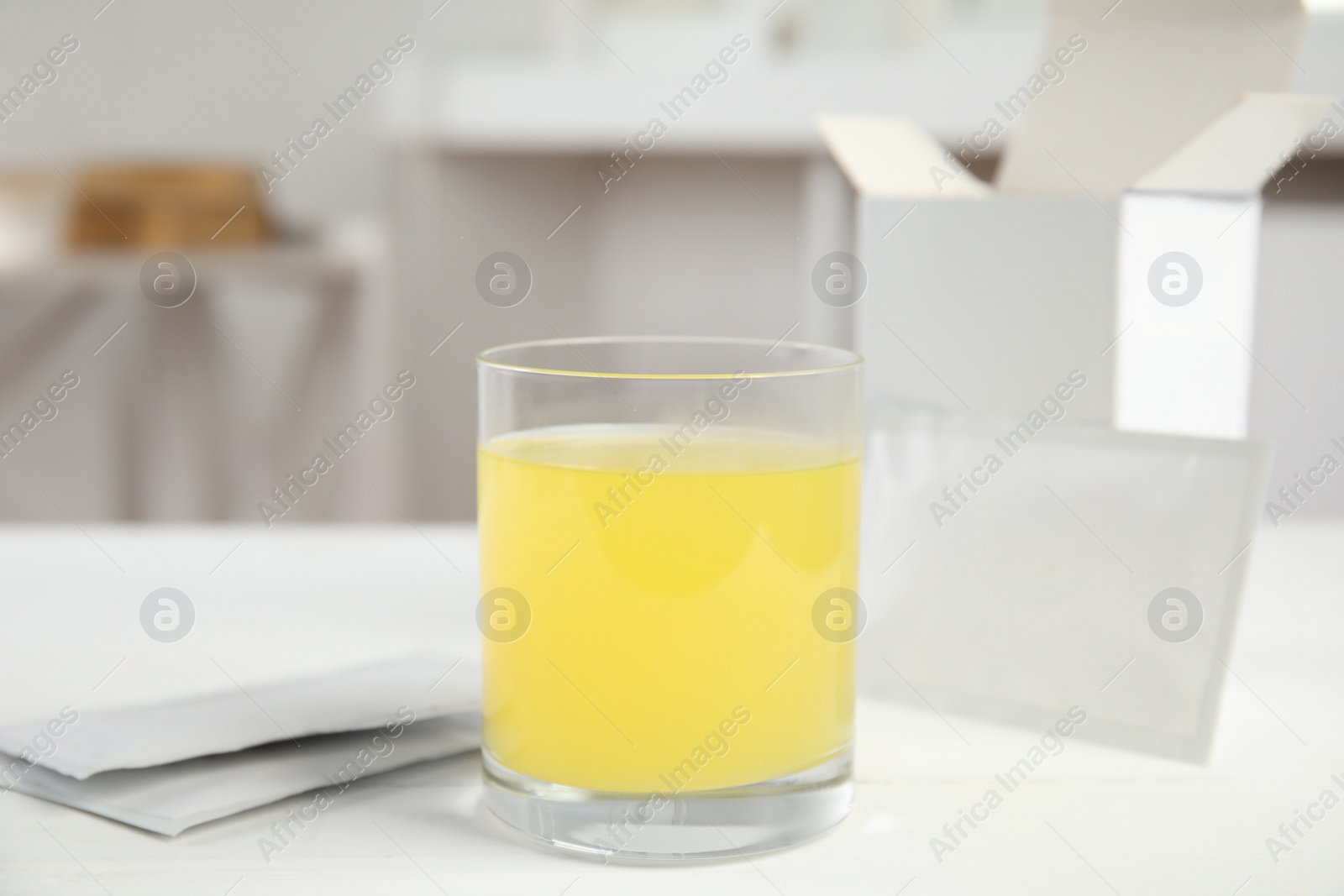 Photo of Glass with dissolved drug and medicine sachets on table indoors