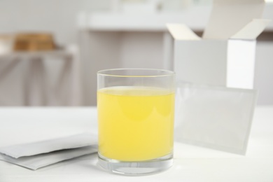 Glass with dissolved drug and medicine sachets on table indoors