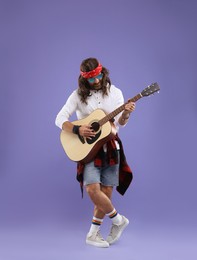 Photo of Stylish hippie man in sunglasses playing guitar on violet background