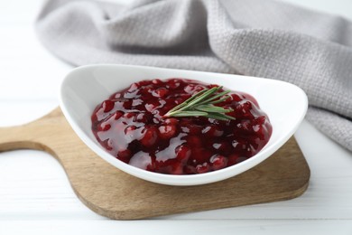 Photo of Fresh cranberry sauce and rosemary in bowl on white wooden table, closeup