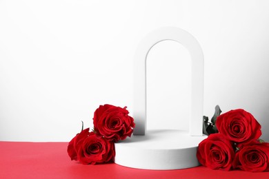 Photo of Stylish presentation for product. Geometric figures and roses on red table against white background, space for text