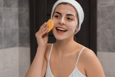 Young woman with headband washing her face using sponge in bathroom