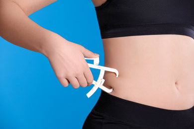 Photo of Young woman measuring body fat with caliper on blue background, closeup. Nutritionist's tool