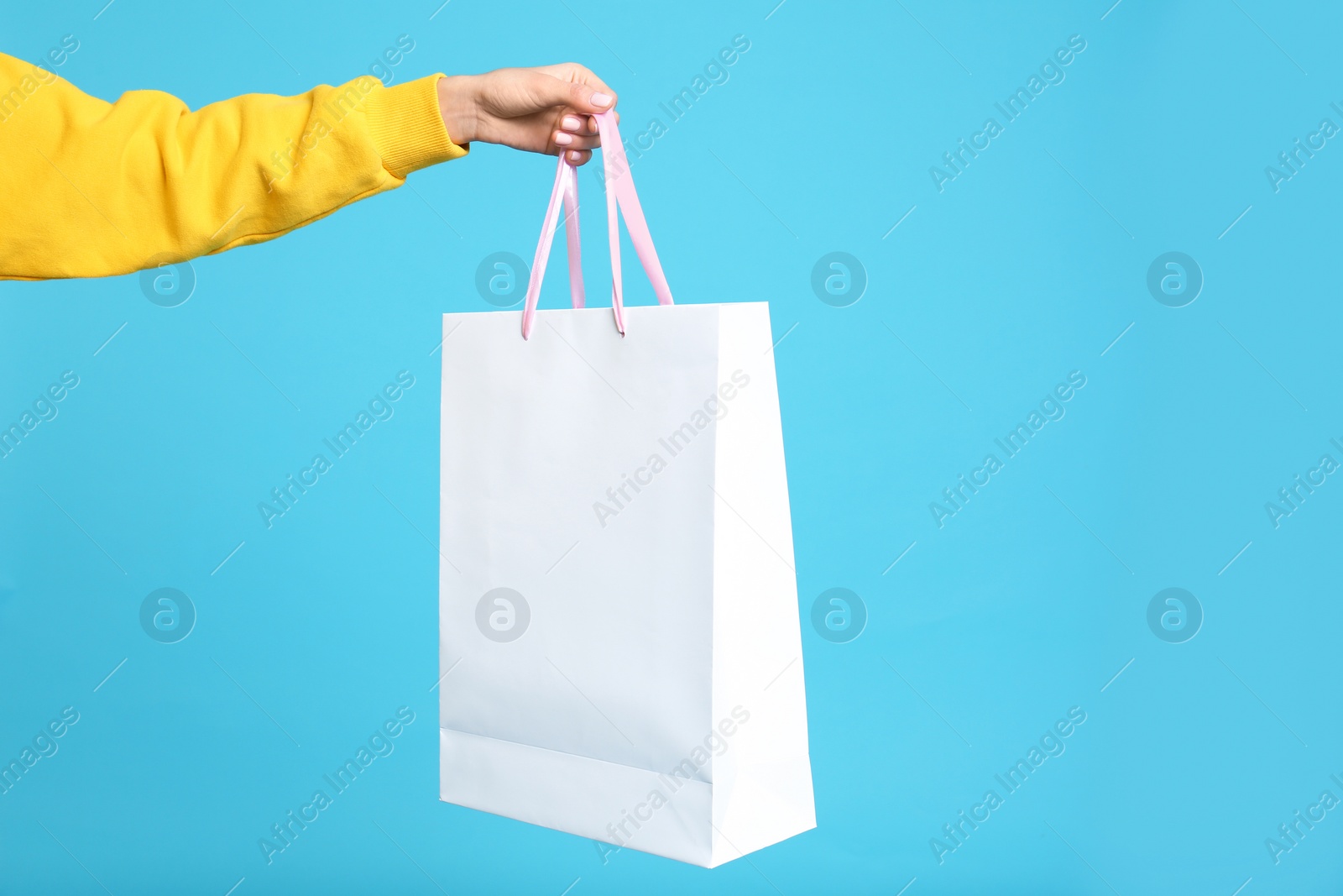 Photo of Young woman holding paper bag on blue background, closeup
