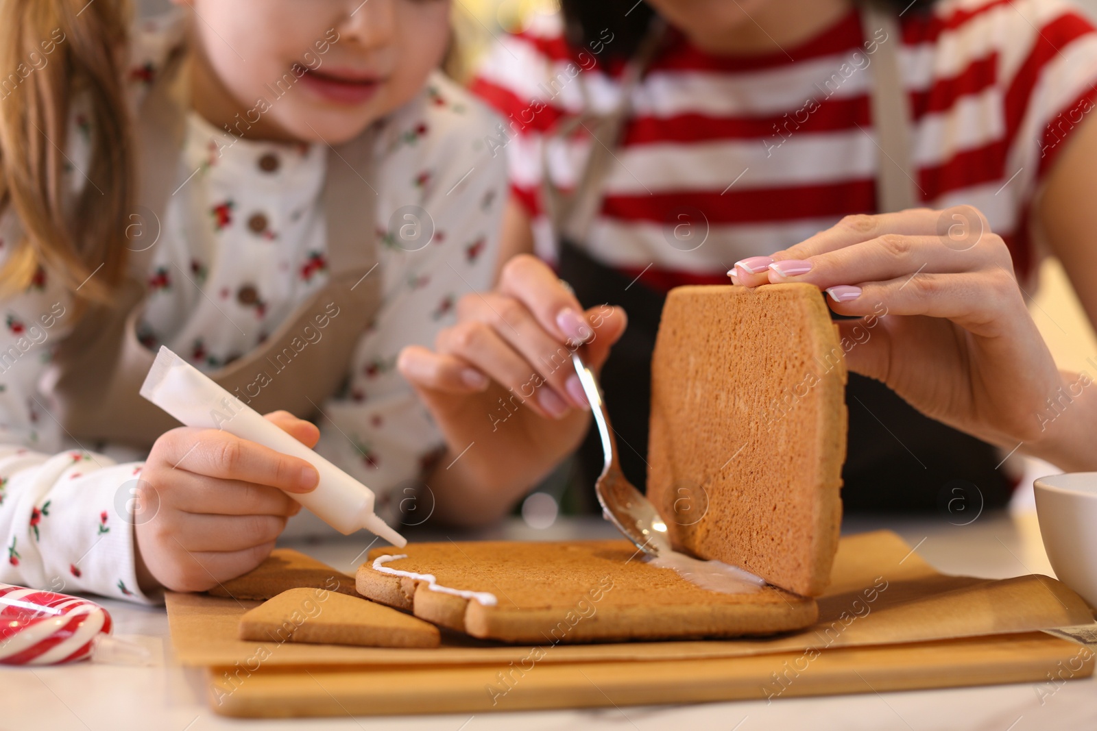 Photo of Mother and daughter making gingerbread house at table, closeup