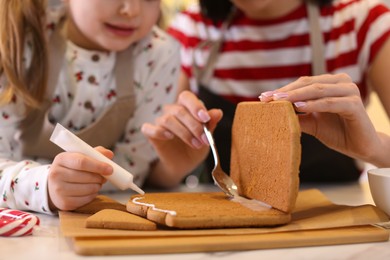 Mother and daughter making gingerbread house at table, closeup