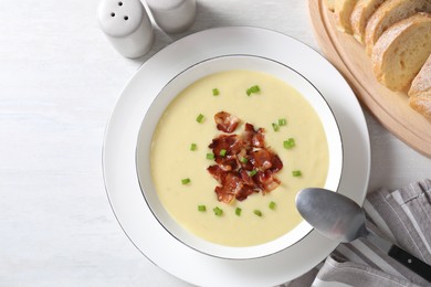 Photo of Tasty potato soup with bacon in bowl served on white wooden table, flat lay