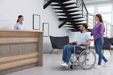Woman with man in wheelchair near receptionist at clinic