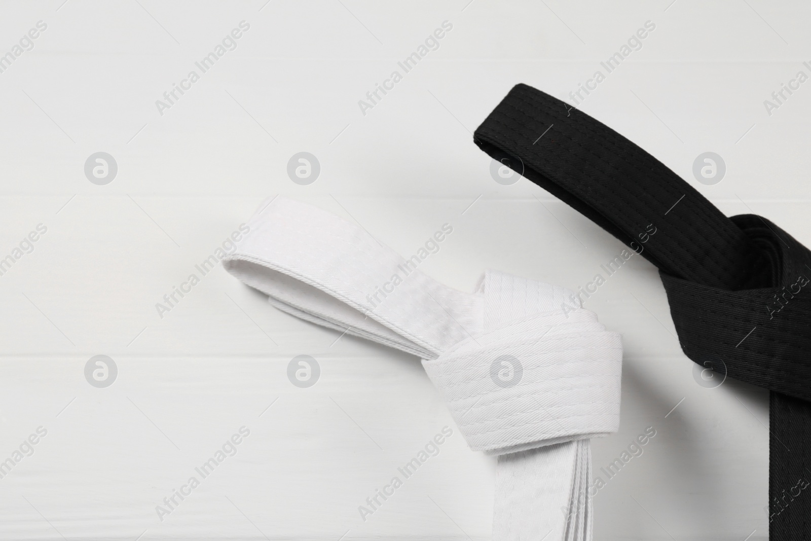 Photo of Black and white karate belts on wooden background, flat lay