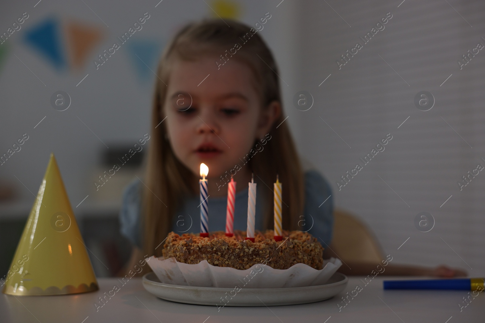 Photo of Cute girl with birthday cake at table indoors, focus on candles