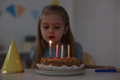 Photo of Cute girl with birthday cake at table indoors, focus on candles