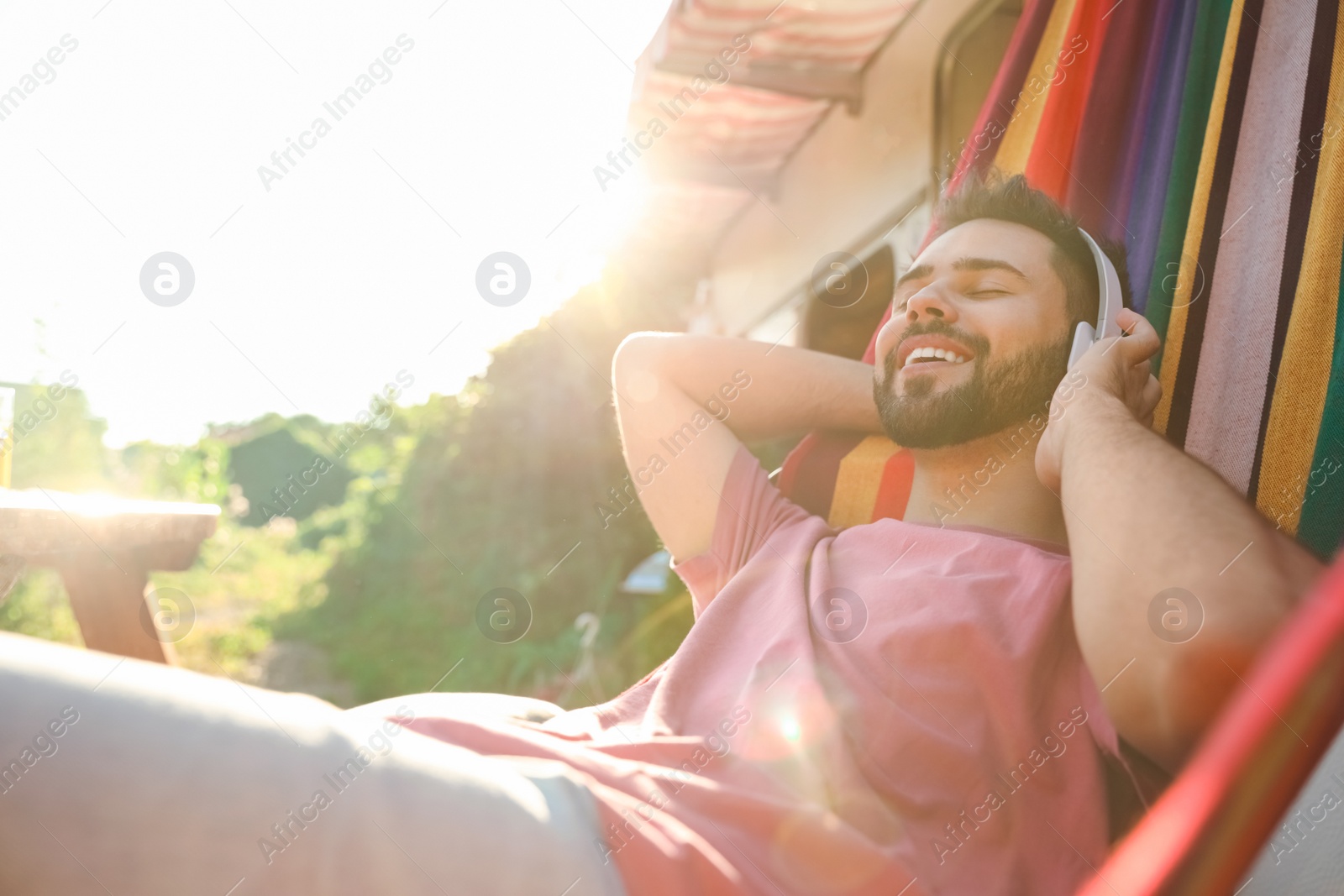 Photo of Young man listening to music in hammock near motorhome outdoors on sunny day