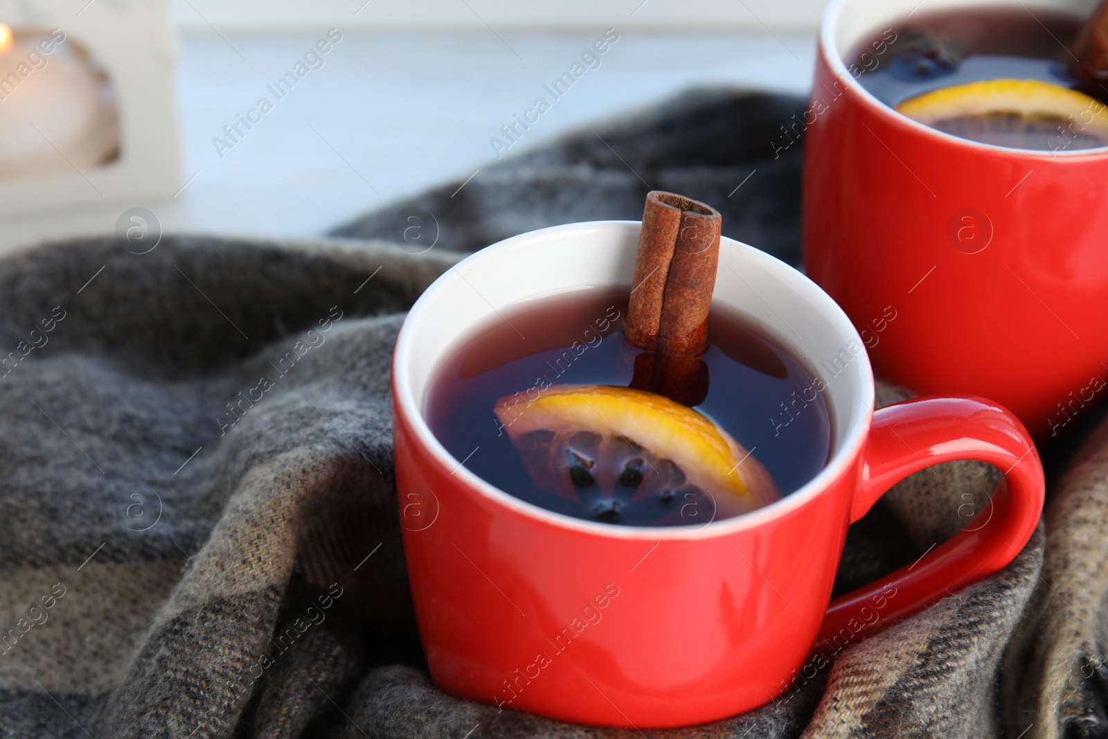 Photo of Cups of hot winter drink with scarf on table, closeup