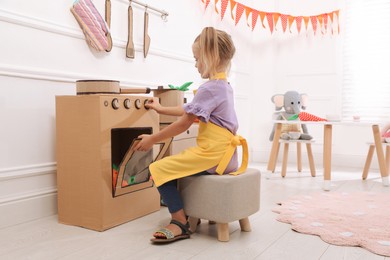 Photo of Little girl playing with toy cardboard oven at home