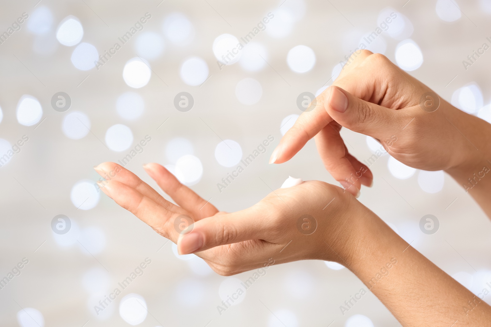 Photo of Woman applying hand cream on blurred background, closeup