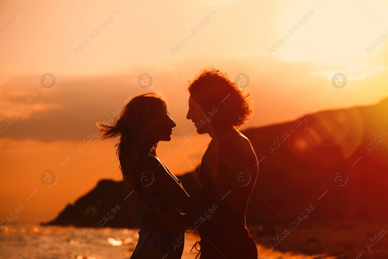 Photo of Young woman in bikini and her boyfriend on beach at sunset. Lovely couple