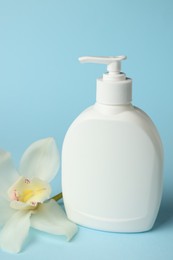 Bottle of liquid soap and flower on light blue background