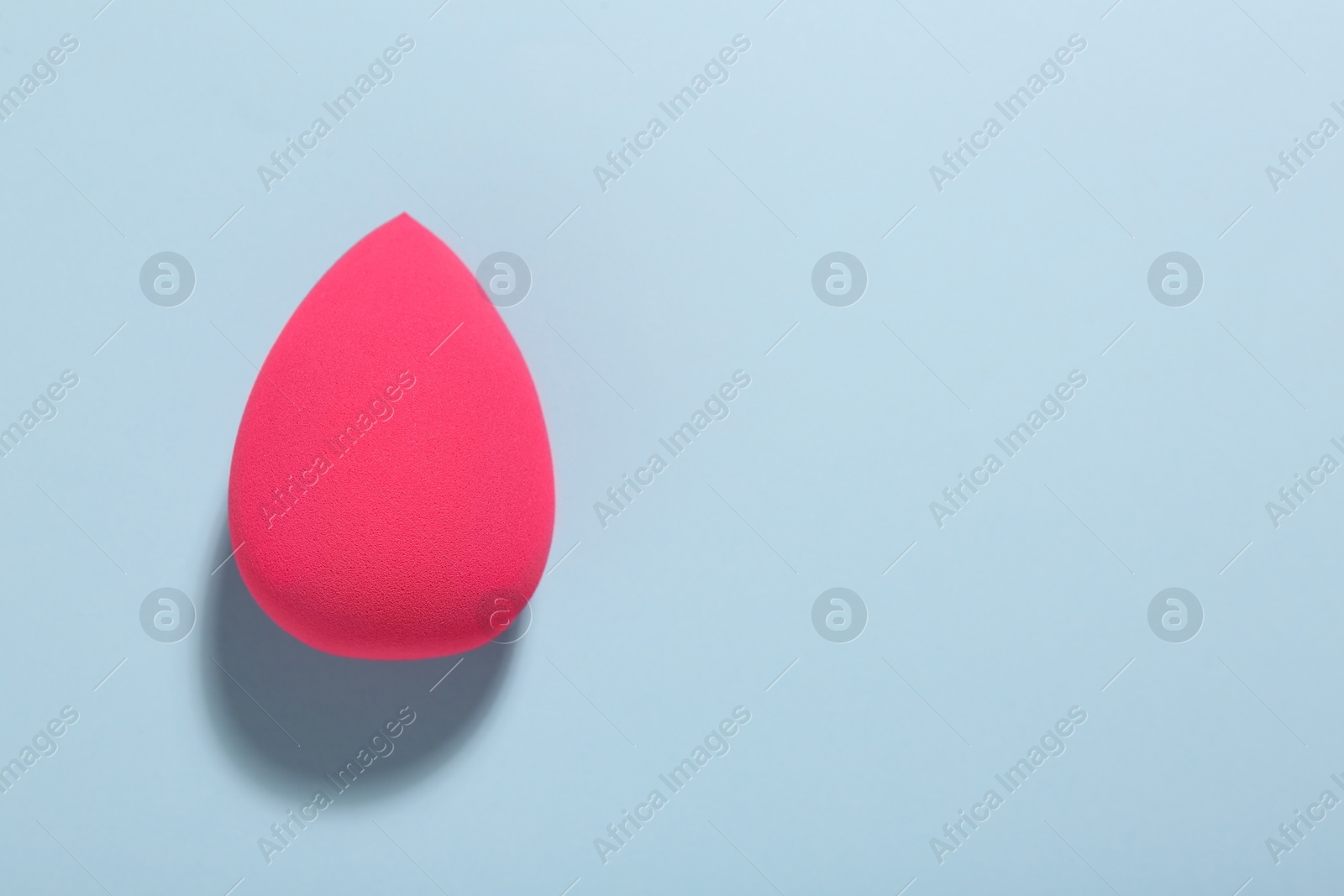 Photo of Pink makeup sponge on light blue background, top view. Space for text