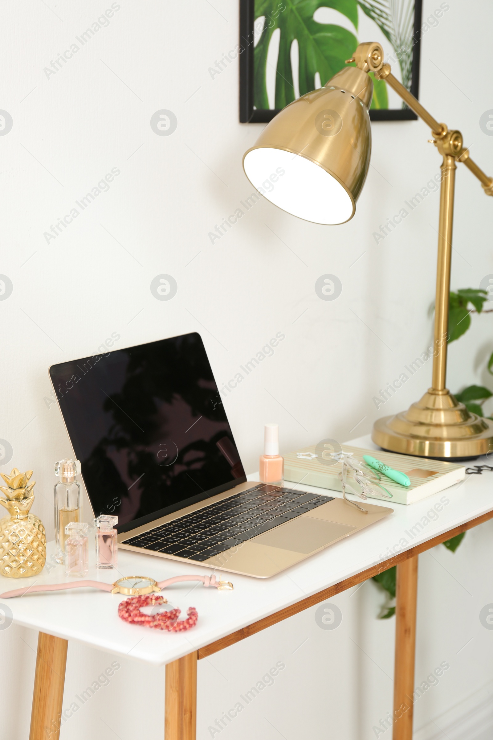 Photo of Stylish workplace with modern laptop and cosmetic products on table near light wall. Beauty blogger