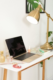 Photo of Stylish workplace with modern laptop and cosmetic products on table near light wall. Beauty blogger