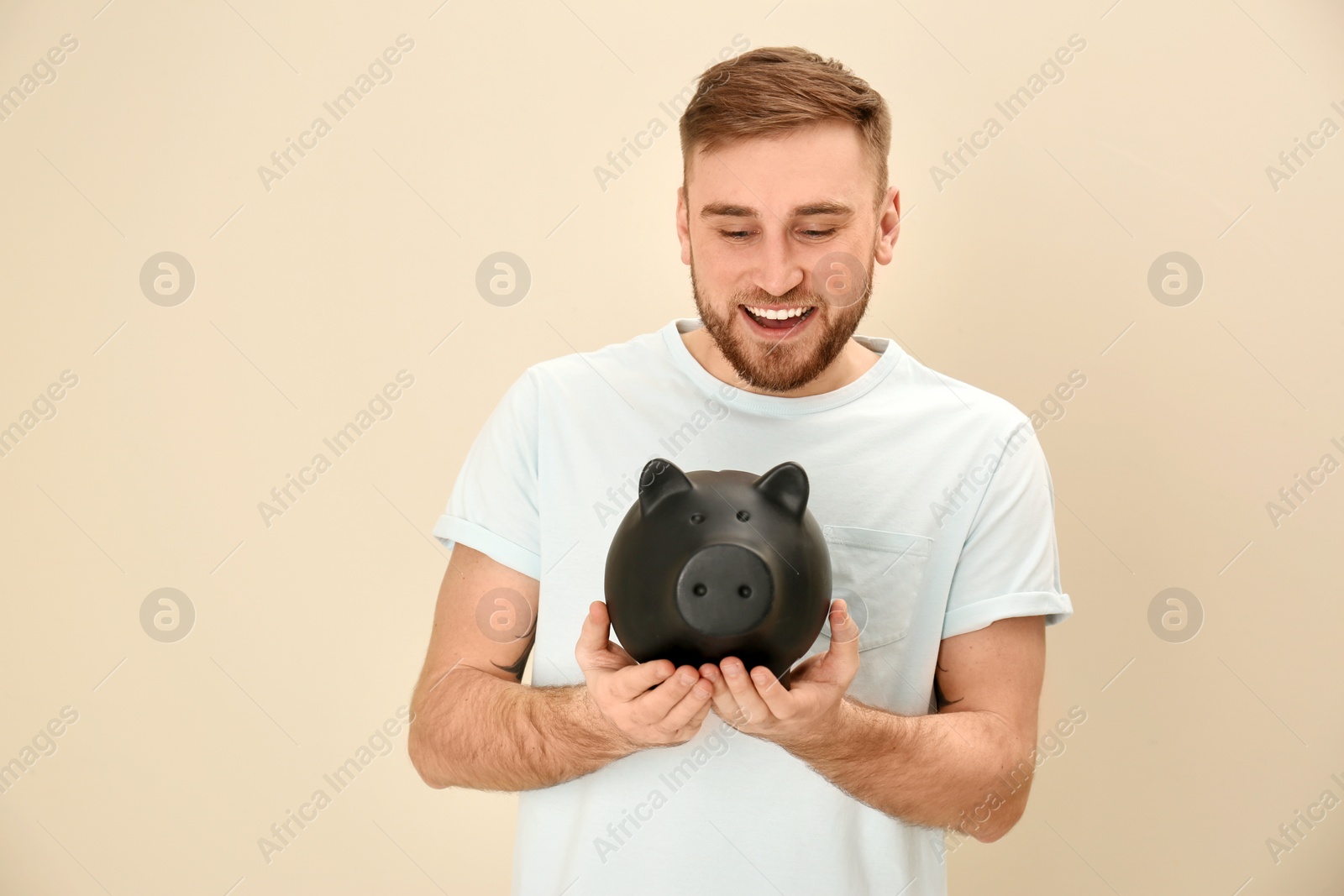 Photo of Portrait of happy young man with piggy bank on color background. Money saving