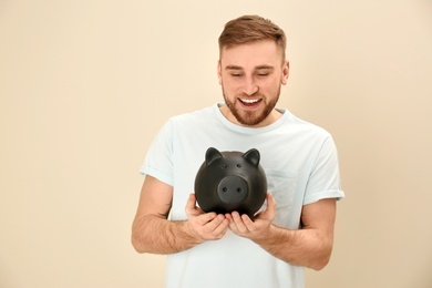 Portrait of happy young man with piggy bank on color background. Money saving