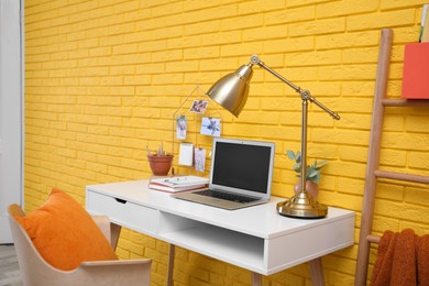 Photo of Stylish home office interior with comfortable workplace near yellow brick wall