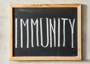 Photo of Chalkboard with word Immunity on light background, top view