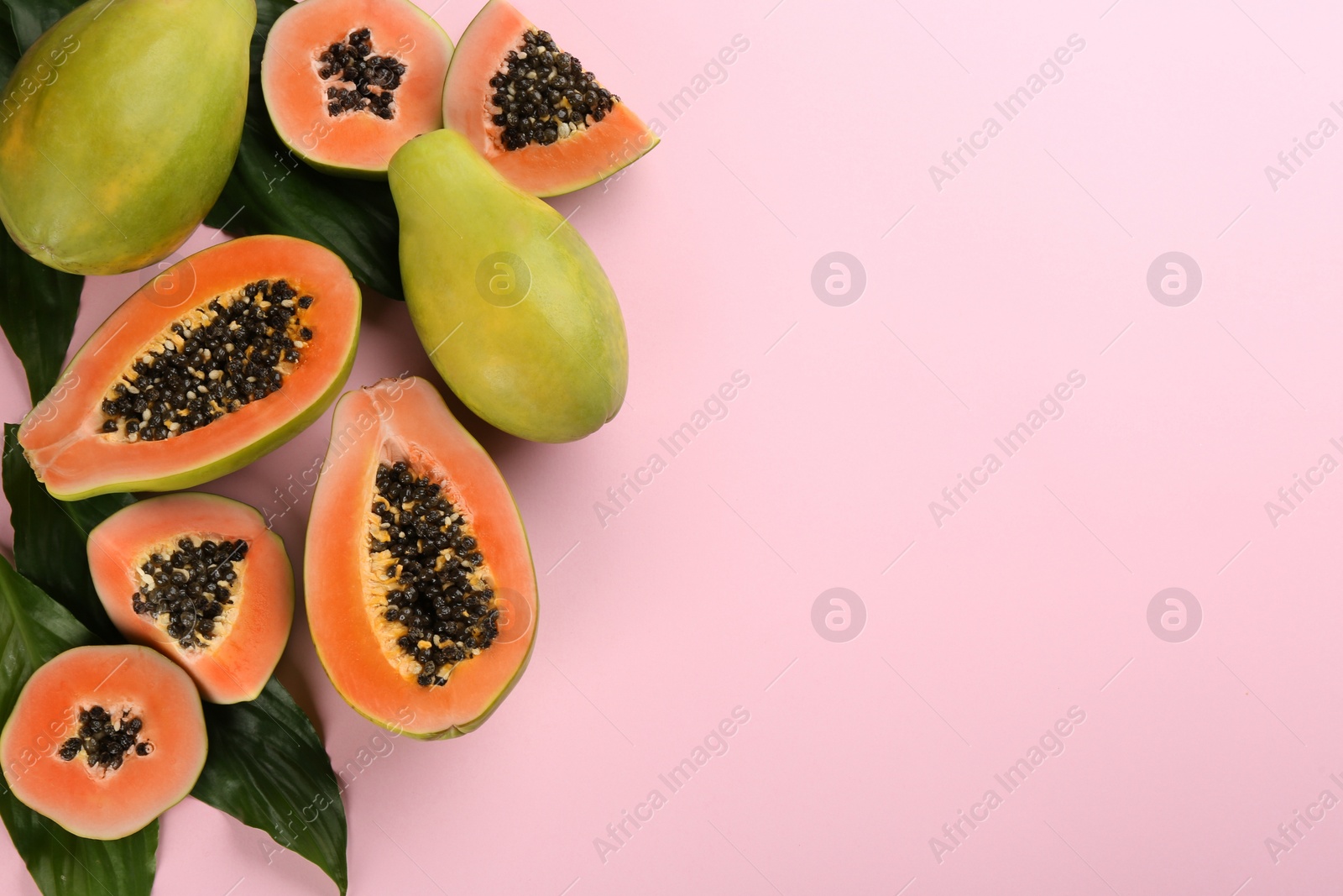 Photo of Fresh ripe papaya fruits with green leaves on pink background, flat lay. Space for text