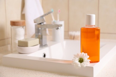 Photo of Fresh mouthwash in bottle and chamomile on sink in bathroom, closeup. Space for text