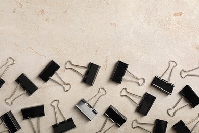 Photo of Black binder clips on light background, flat lay. Space for text