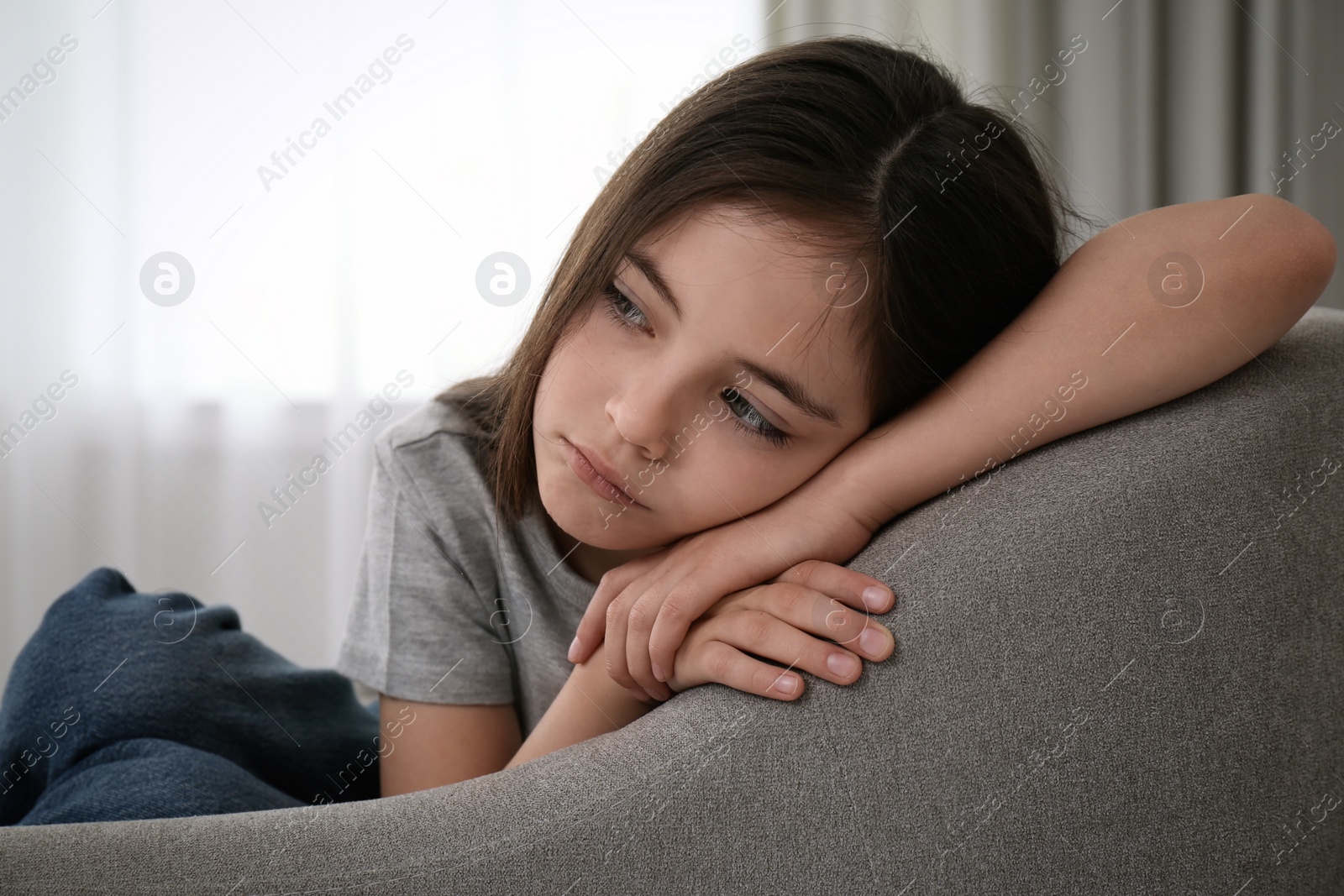 Photo of Sad little girl sitting on sofa indoors