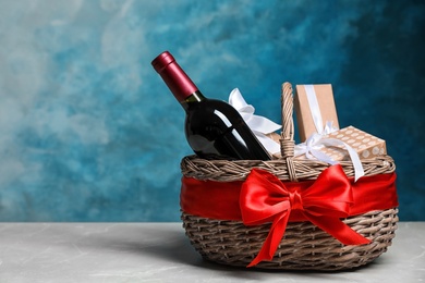 Photo of Gift basket with bottle of wine on color background. Space for text