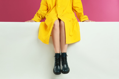 Photo of Woman in stylish boots sitting on color background, closeup