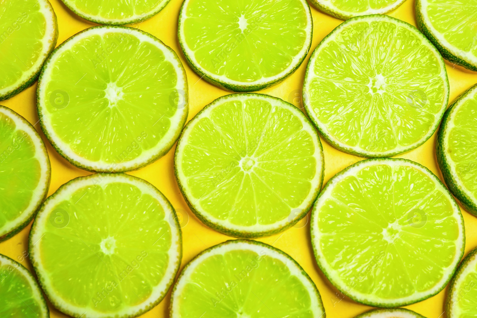 Photo of Juicy fresh lime slices on yellow background, flat lay