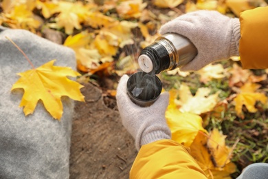 Photo of Woman pouring drink from thermos into cap outdoors, closeup