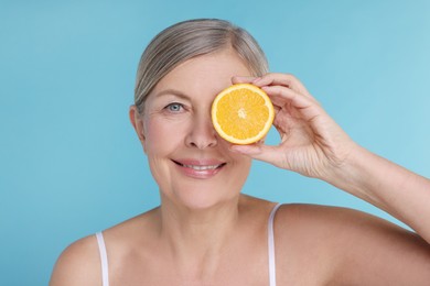 Photo of Beautiful woman with half of orange rich in vitamin C on light blue background