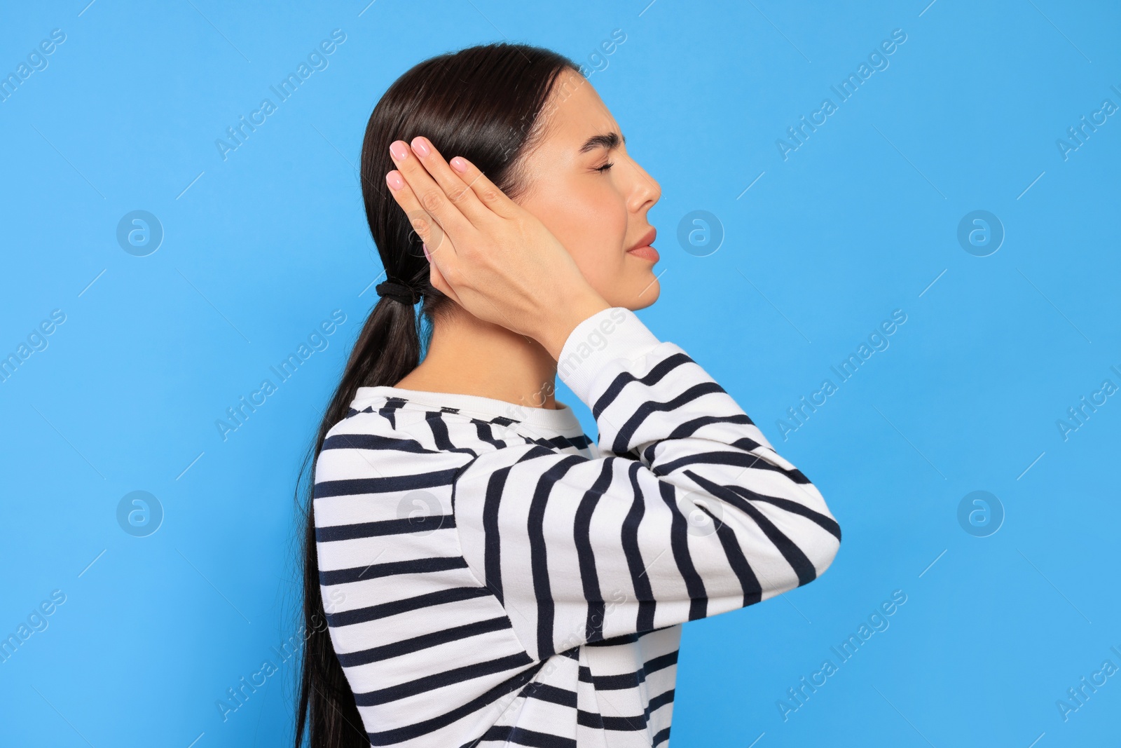 Photo of Young woman suffering from ear pain on light blue background