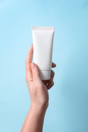 Photo of Woman with tube of hand cream on light blue background, closeup