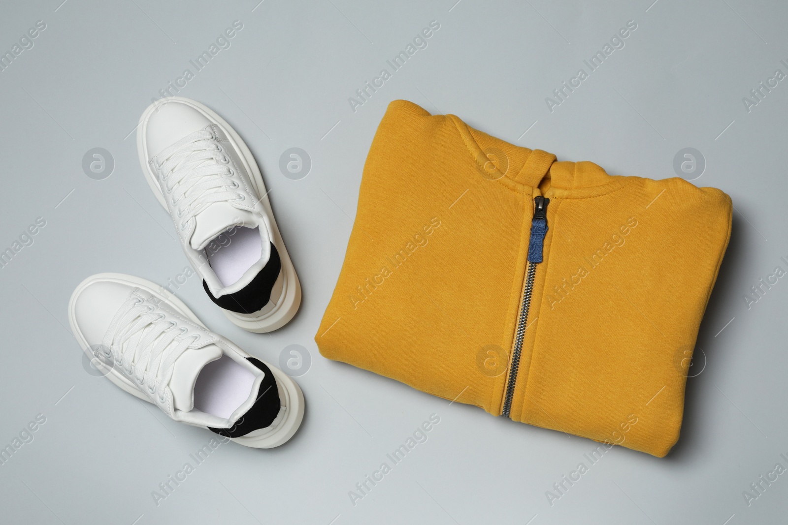 Photo of Yellow garment and sport shoes on grey background, flat lay