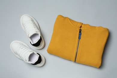 Yellow garment and sport shoes on grey background, flat lay