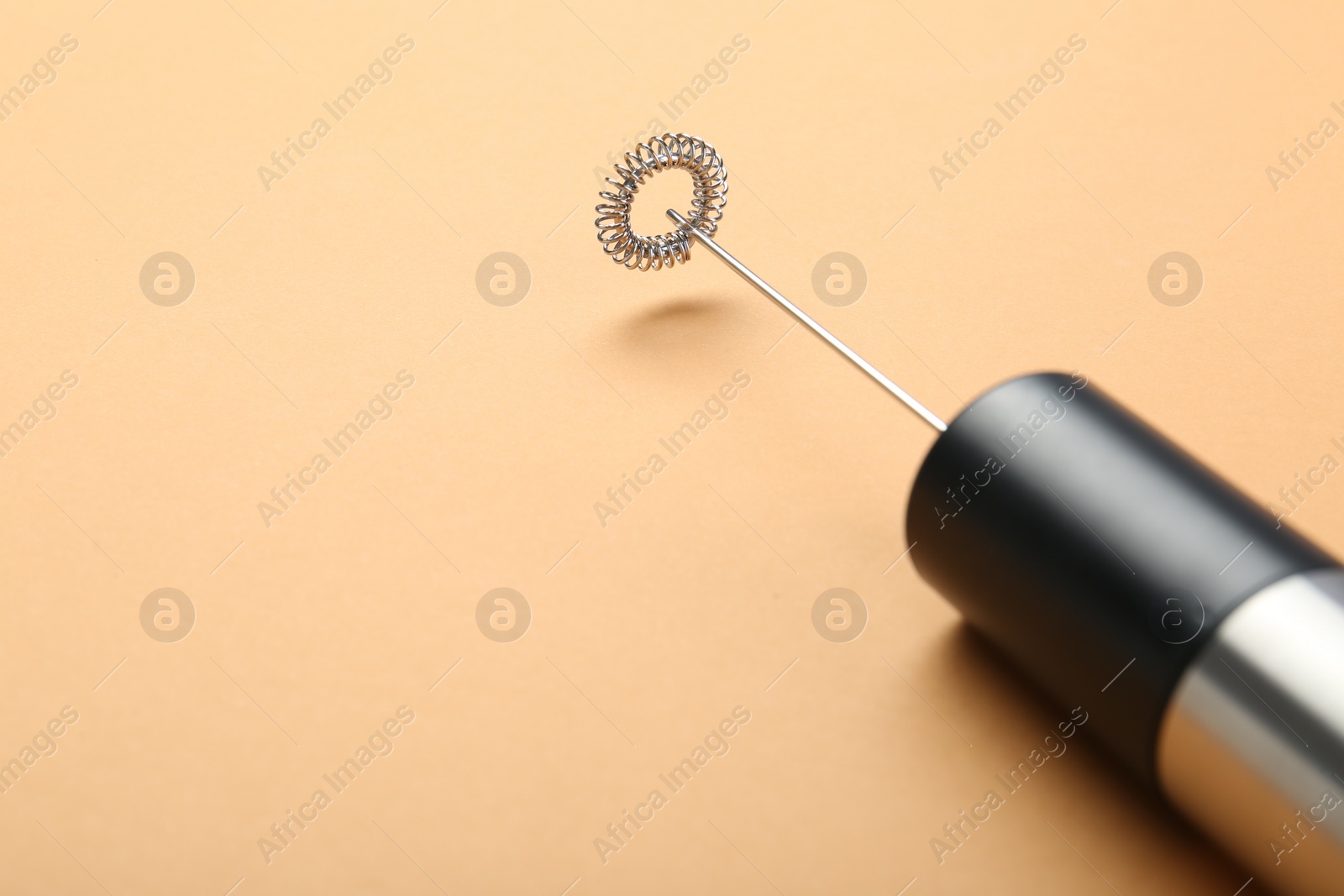 Photo of Milk frother wand on pale orange background, closeup. Space for text