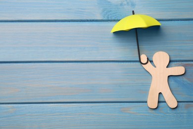 Small umbrella and person figure on light blue wooden background, flat lay. Space for text