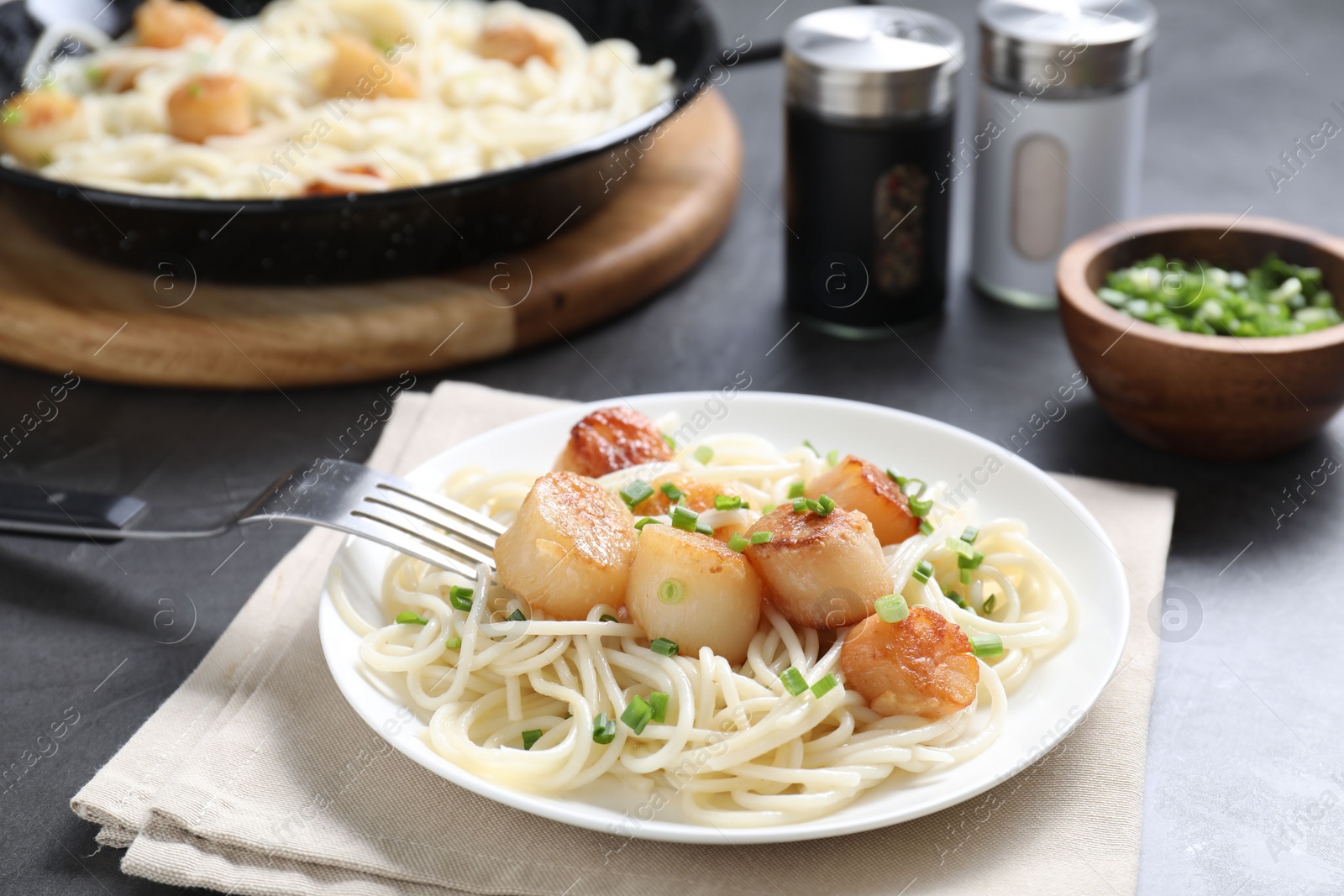 Photo of Delicious scallop pasta with green onion served on grey table