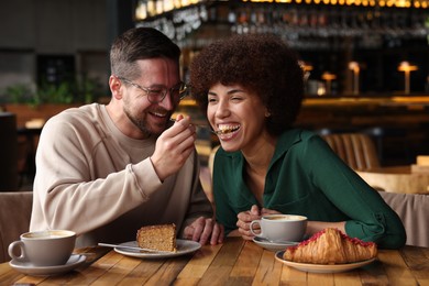 Photo of International dating. Handsome man feeding his girlfriend with cake in cafe
