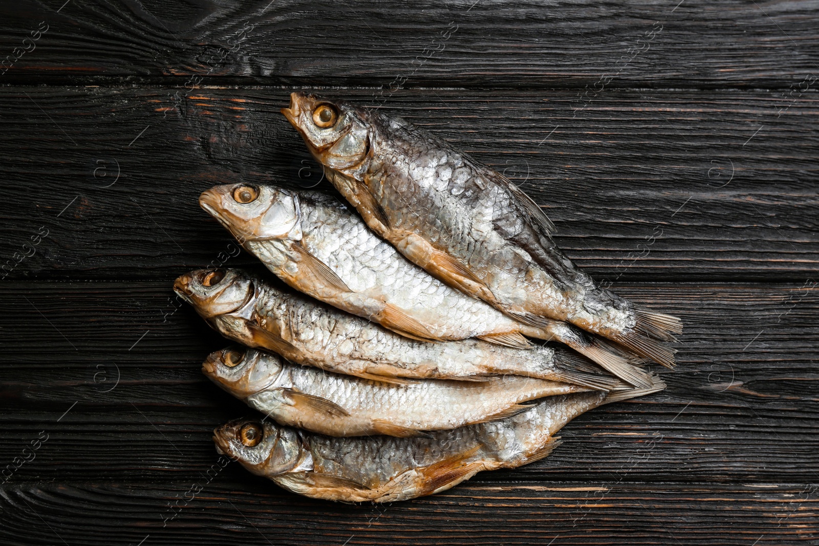 Photo of Tasty dried fish on black wooden table, flat lay