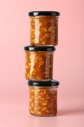 Photo of Tasty salted caramel with peanuts in jars on pink background