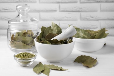 Photo of Whole and ground bay leaves on white wooden table